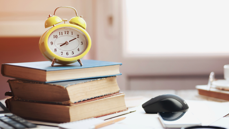 Clock sitting upon books on a desk.